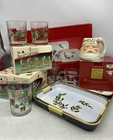 Photo showing Santa Toby mug and box, several Christmas-themed old-fashioned glasses, and lacquer trays with holly decoration.