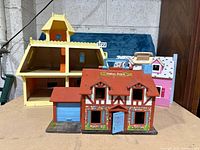 Three dollhouses displayed on a flat surface including Fisher Price Little People, Mattel The Littles Victorian Dollhouse, and Melissa and Doug Fold and Go Play House in the background.