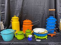 Full set of vintage enamelware cookware including pots, pans, teapots, milk canister, creamer, tiffin box, and trivets in various colors.