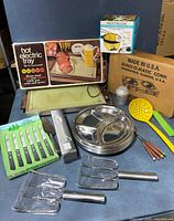 Photo showing an assortment of vintage kitchen items including aluminum divided plates, boxed hot electric tray, boxed popcorn popper, boxed knives, coffee filter box, and various utensils.