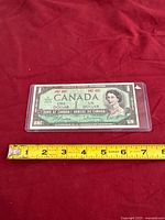 Full view of commemorative $1 banknote in sleeve with tape measure for size