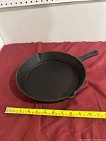 Top view of cast iron frying pan showing cooking surface and handle with measuring tape displaying length