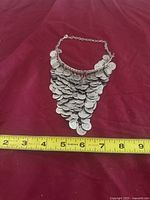 Full view of coin bib necklace with measuring tape for scale