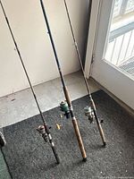 Three fishing rods with reels standing upright on carpet