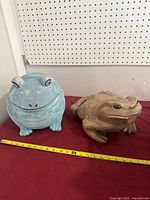 Front view of both frog statues on table with tape measure for scale