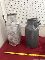 Both milk cans side by side with measuring tape for scale