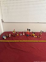 Group shot of all figurines aligned on red surface with measuring tape for scale