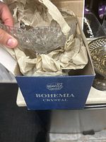 Clear Bohemia crystal glass bowl shown inside its original branded blue box with protective paper wrapping, held in hand.