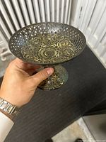 Photo showing the side and inside of the etched brass bowl with inlaid gold-tone floral pattern held in hand.