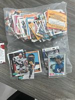 Photo showing a large plastic bag filled with loose sports trading cards along with three cards placed outside the bag, including hockey and baseball cards.