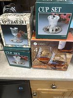 Three boxed sets visible: two ornate metal cup sets with floral engraving and one box of four Libbey Madison Whiskey glasses.