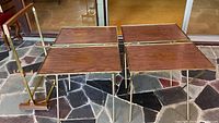 Four folding tray tables with veneer tops and brass-tone legs, shown standing with wheeled caddy