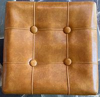 Top view of ottoman showing brown leatherette surface, four buttons, stitched grid pattern