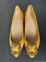Top down photo of yellow satin Manolo Blahnik ballerina flats showing crystal buckles on pointed toe and labeled insole.