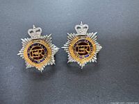 Pair of vintage metal badges with crowns and starburst designs on a dark surface.
