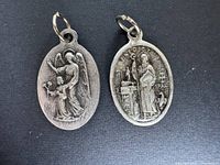 Photo of two oval religious pendants, one depicting an angel comforting a child and the other showing a saint at an altar with inscriptions