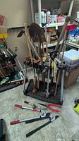 Full lot showing assorted long-handle tools in holder and handheld tools on floor