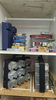 Wide view of two shelves showing blue cases, blue-lid containers, red-lid bin, hardware packs and rack with small boxes