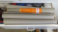 Drawer with four gray Grip Premium shelf liner rolls on top of assorted tapes