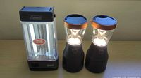 Coleman lantern and two Duracell lanterns illuminated on tabletop
