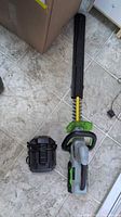 Hedge trimmer with blade cover beside charger