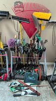 Front view of wheeled stand holding variety of long-handled yard tools and accessories with small hand tools at base