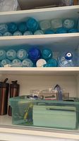 Shelves showing multiple turquoise water bottles, large jug, bronze insulated bottles, storage tote and small box
