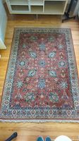 Full view of rust red floral wool area rug on hardwood floor