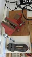 Red swivel bench vise on board, gray clamp vise below
