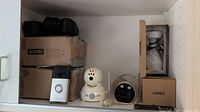 Shelf with ZOSI boxes, coiled cables, Ring doorbell, white PTZ camera, black dome camera, Lorex boxes
