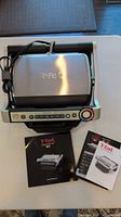 Closed T-fal OptiGrill appliance with attached power cord shown above the three booklets