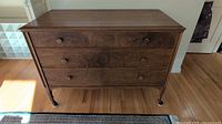 Front view of dark wood dresser showing three drawers and turned castered legs