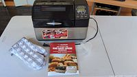 Bread maker with accessories, mitt, manual, measuring cup visible