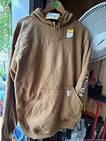 Brown Carhartt hooded sweatshirt hanging, front view showing kangaroo pocket and sleeve logo