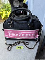 Front view of black and pink Juicy Couture bowler handbag with chain strap and logo graphics