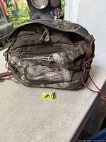 Front view of Ozark Trail camouflage waistpack showing main zip compartments, brand logo patch, mesh front pocket and red shock cords
