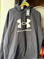 Front view of black Under Armour hoodie on hanger showing logo and pocket