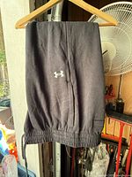 Front view of dark charcoal Under Armour sweatpants on hanger showing embroidered logo and waistband