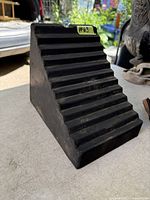 Angled view of black solid rubber wheel chock showing ridged incline