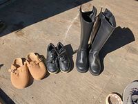 Three pairs of footwear on floor: tan clogs, black sneakers, black tall boots