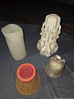 Group shot of four candles: ivory pillar, carved candle, red candle in pot, small candle under cloche