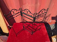 Full view of three-panel black metal jewelry stand on red surface