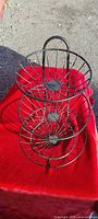 Full view of three-tier black metal wire fruit basket stand on red cloth