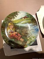 Plate with girl seated by stream placed on packaging sheet