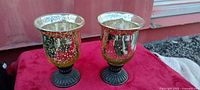 Front view of two mercury glass urn candle holders on red cloth