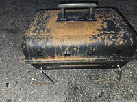 Closed grill showing rusted lid and folding legs