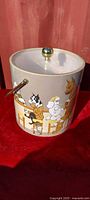 Front view of ice bucket with lid on showing illustrated dogs and brass knob