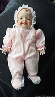 Full view of porcelain baby doll wearing pink romper and bonnet