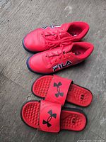 Pair of red FILA sneakers and red Under Armour slides displayed side by side