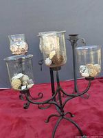 Full view of wrought iron candle stand with three hanging glass hurricanes